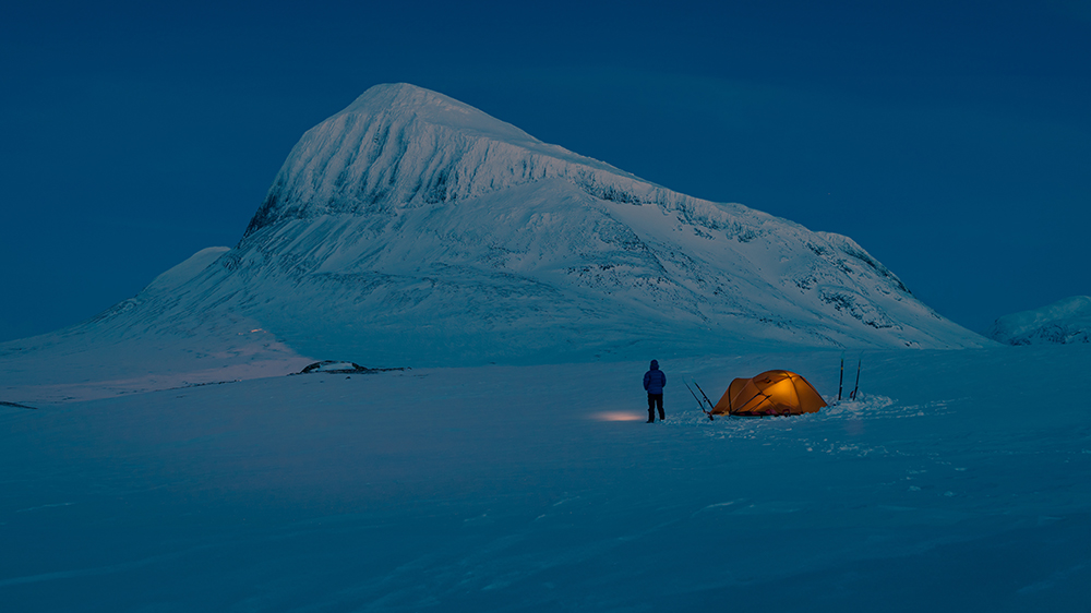 Adventurer beside her tent in the winter landscape of National Park Sarek, Lapland.